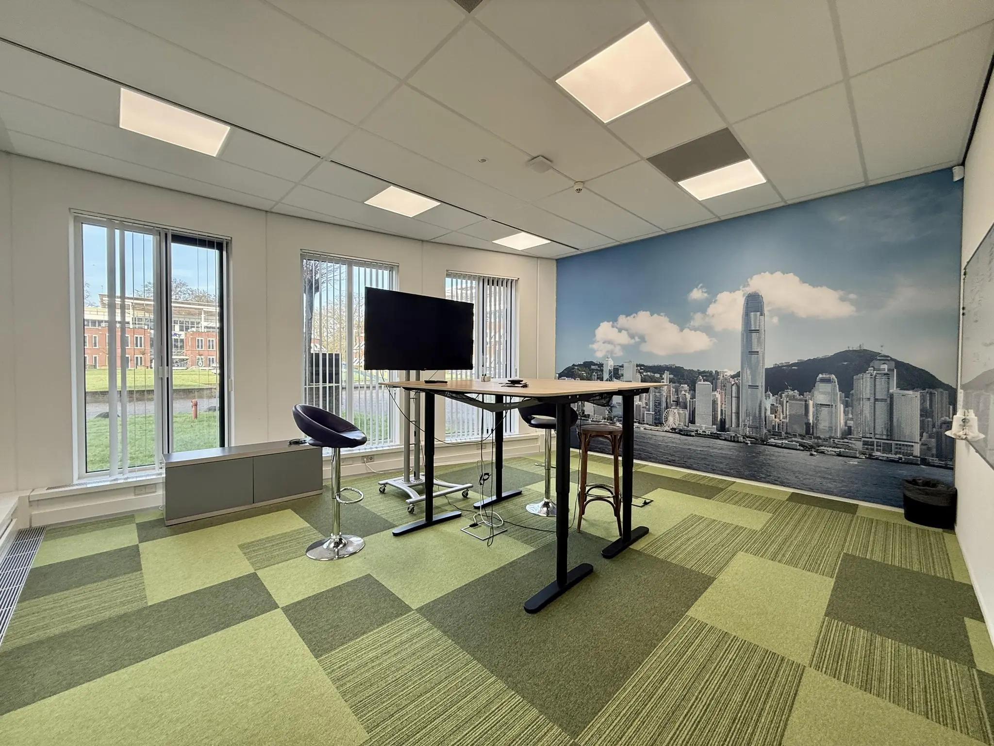 Moderne vergaderruimte aan de Arnhemse Bovenweg met hoge tafels, barkrukken, groot scherm en een wanddecoratie van de skyline van Hongkong.